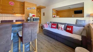 Ein gemütliches Zimmer mit einer Holzeinrichtung, einer Couch mit Ski-Kissen, einer Mikrowelle und einer Kaffeemaschine.