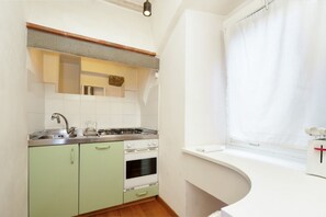 Una cocina compacta con estufa a gas, horno y lavamanos, y una ventana con cortina blanca.