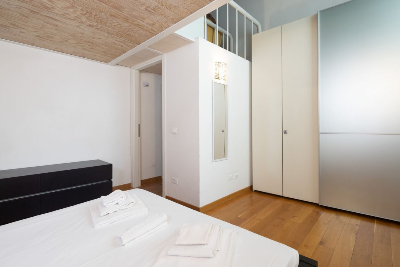 Ein Schlafzimmer mit einem Bett, einer schwarzen Kommode, einem Kleiderschrank und einem Spiegel.