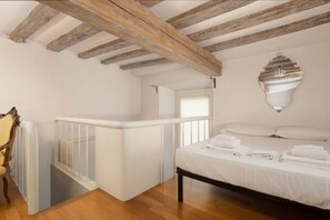 Un dormitorio con techo de madera, cama blanca y sábanas ordenadas, y barandilla blanca.