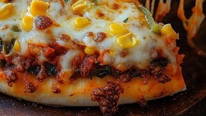 Primer plano de una pizza con ingredientes visibles como queso, maíz y pimientos verdes.