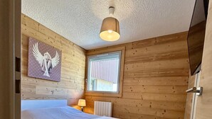 A bedroom with a bed, a window, a wall-mounted TV, and a ceiling light. - Appartement-pied des pistes -T3 -60 m2 -Garage _ Free WFI - Resort center (Les Deux Alpes)