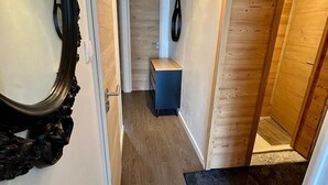 A narrow hallway with wooden flooring, a blue bench, a black mirror, and a ceiling light fixture. - Appartement-pied des pistes -T3 -60 m2 -Garage _ Free WFI - Resort center (Les Deux Alpes)
