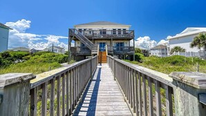 A wooden boardwalk leading to a two-story beachfront building with balconies.