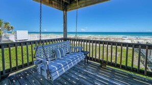 A wooden deck with a swing chair overlooking a beach.
