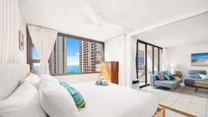 A hotel room with a bed, a sofa, a desk, and a view of the sea.