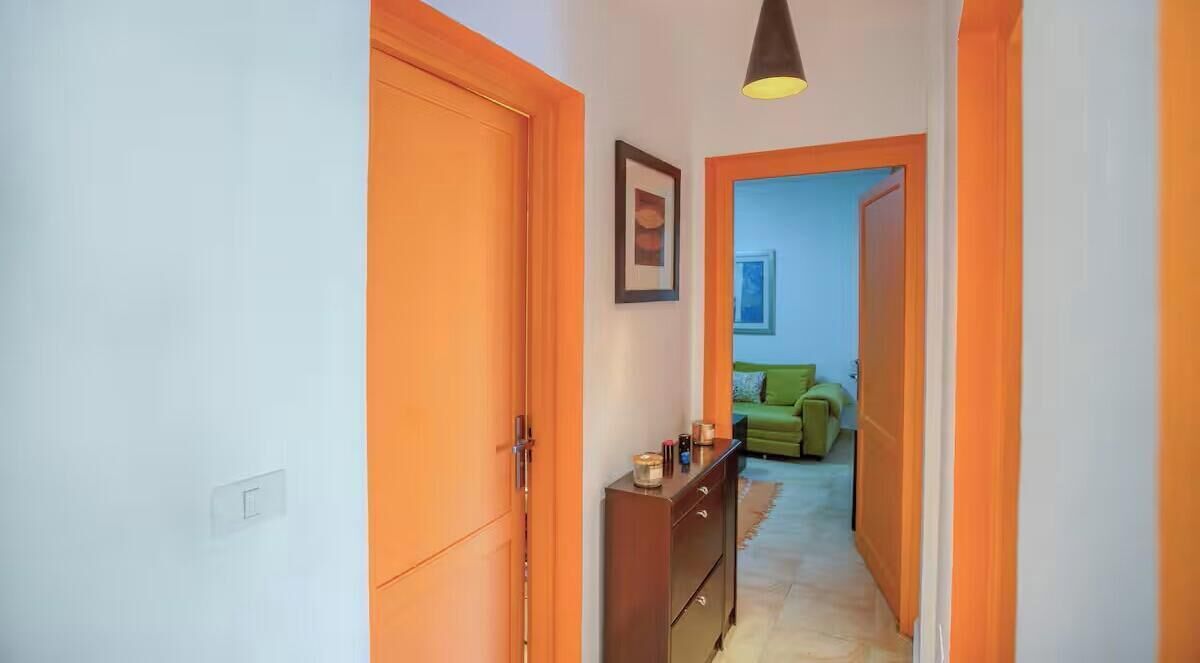 A hallway with orange doors leading to a room with a green sofa and a framed picture on the wall.