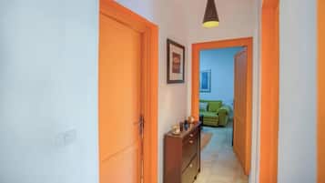 A hallway with orange doors leading to a room with a green sofa and a framed picture on the wall.