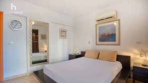 A modern hotel room with a large bed, a nightstand, a wall-mounted air conditioner, and a framed picture above the bed. - Comfy Apartment in Rehab City (New Cairo)