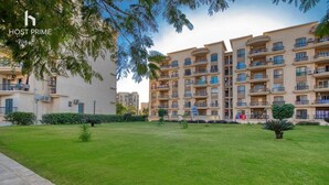 A multi-story residential building with balconies, a well-maintained lawn, and a clear sky. - Comfy Apartment in Rehab City (New Cairo)
