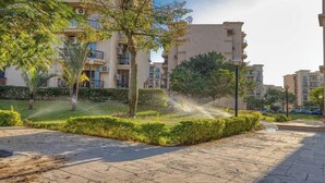 A residential building with balconies, a well-maintained garden, and a paved walkway. - Comfy Apartment in Rehab City (New Cairo)