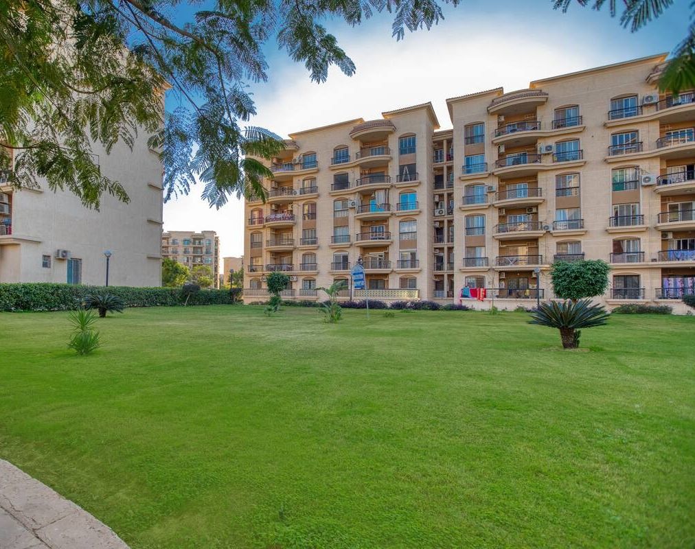 Um edifício residencial com vários andares, varandas, um gramado bem cuidado e céu claro.