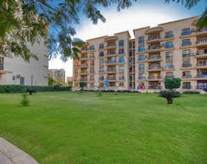 Um edifício residencial com vários andares, varandas, um gramado bem cuidado e céu claro.