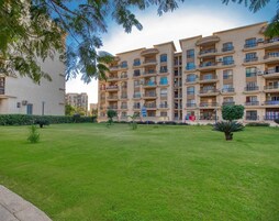 A multi-story residential building with balconies, a well-maintained lawn, and a clear sky.