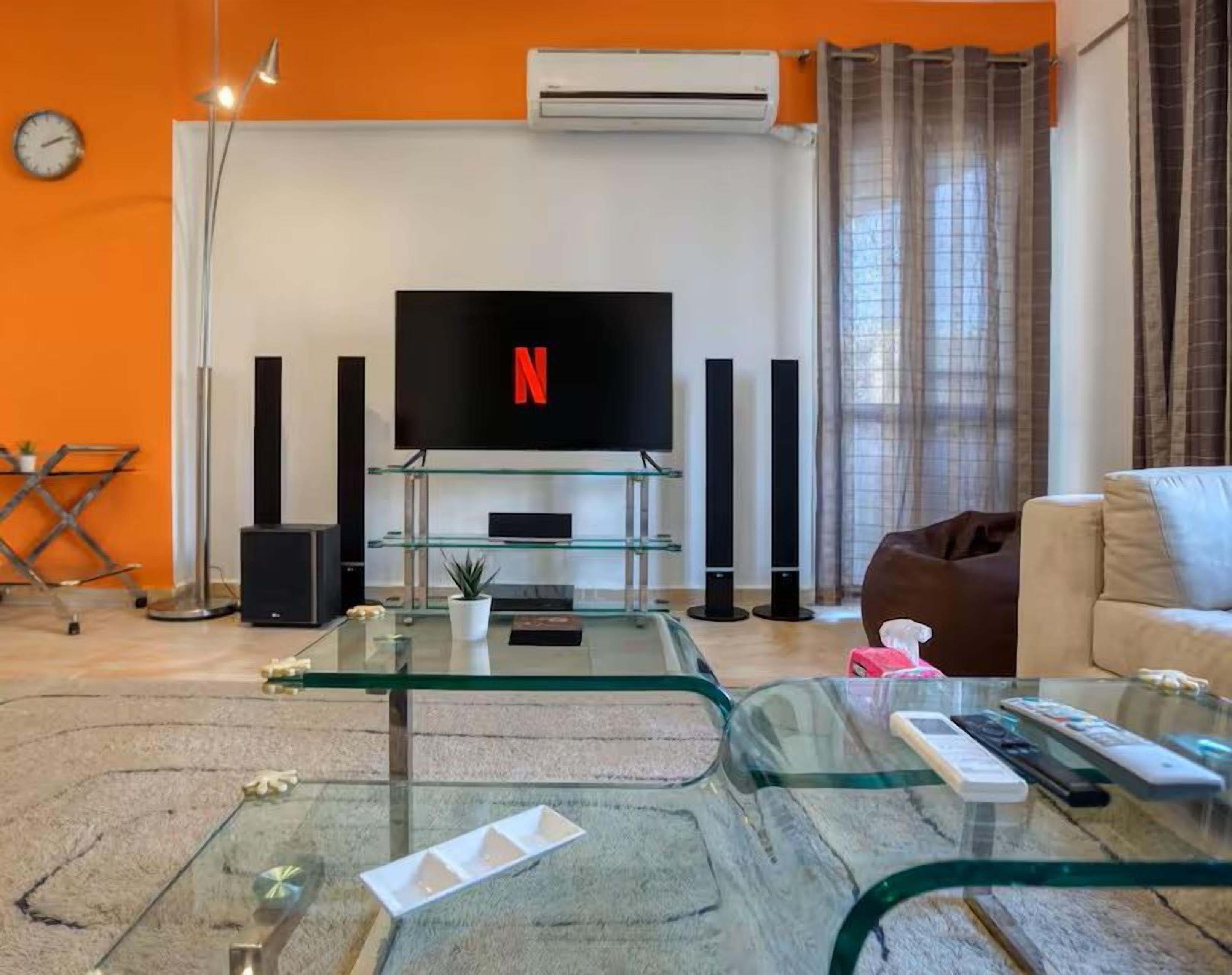 A modern living room with a glass coffee table, a flat-screen TV, and a sofa.