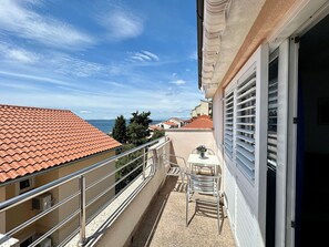 En balkon med et bord og stole, der kigger ud over et kystområde med røde tage og en klar himmel.