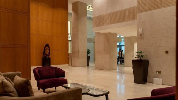 Un hall d’entrée spacieux, avec un fauteuil rouge, une table basse en verre et un mur décoratif en bois.