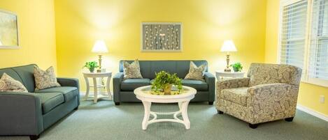 A living room with two sofas, a patterned armchair, a coffee table with a plant, and two side tables with lamps.