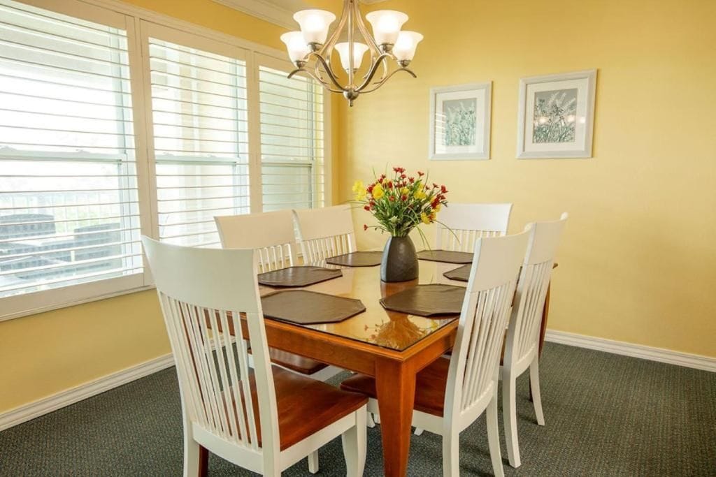 A dining area with a wooden table, white chairs, a chandelier, and a vase of flowers.