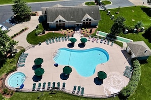 A large swimming pool with lounge chairs and umbrellas, surrounded by a well-maintained lawn and a building with a sloped roof. - Spacious 2BR Getaway at Palace View Heights with Full Resort Amenities (Branson)
