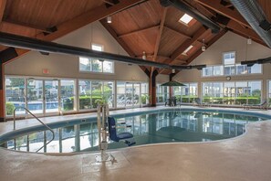 An indoor swimming pool with clear glass walls, a wooden ceiling, and a view of the outdoors. - Escape to Branson | Pools, Sauna, Game Room & Just Minutes from Branson Strip (Branson)