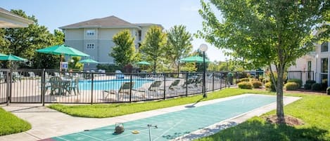 Un espace piscine comprenant un terrain de jeu de palet, des chaises longues et des parasols.