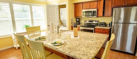 A kitchen with granite countertops, wooden cabinets, stainless steel appliances, and a dining area with chairs and a table.