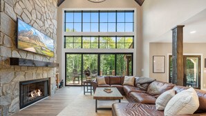 Un salón amplio con chimenea de piedra, sofá de cuero y ventanas grandes que ofrecen vistas al exterior.