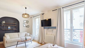 Une chambre d’hôtel moderne équipée d’un canapé, d’une table basse, d’un lit, d’une télévision et de grandes fenêtres avec des rideaux.