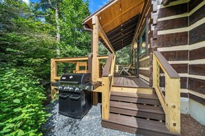 Een houten terras met een barbecue en een zwarte opbergcontainer.