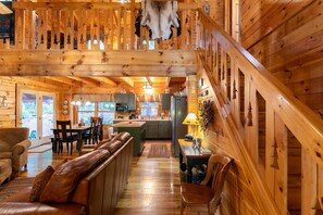 A wooden cabin interior with a dining area, kitchen, and a staircase.