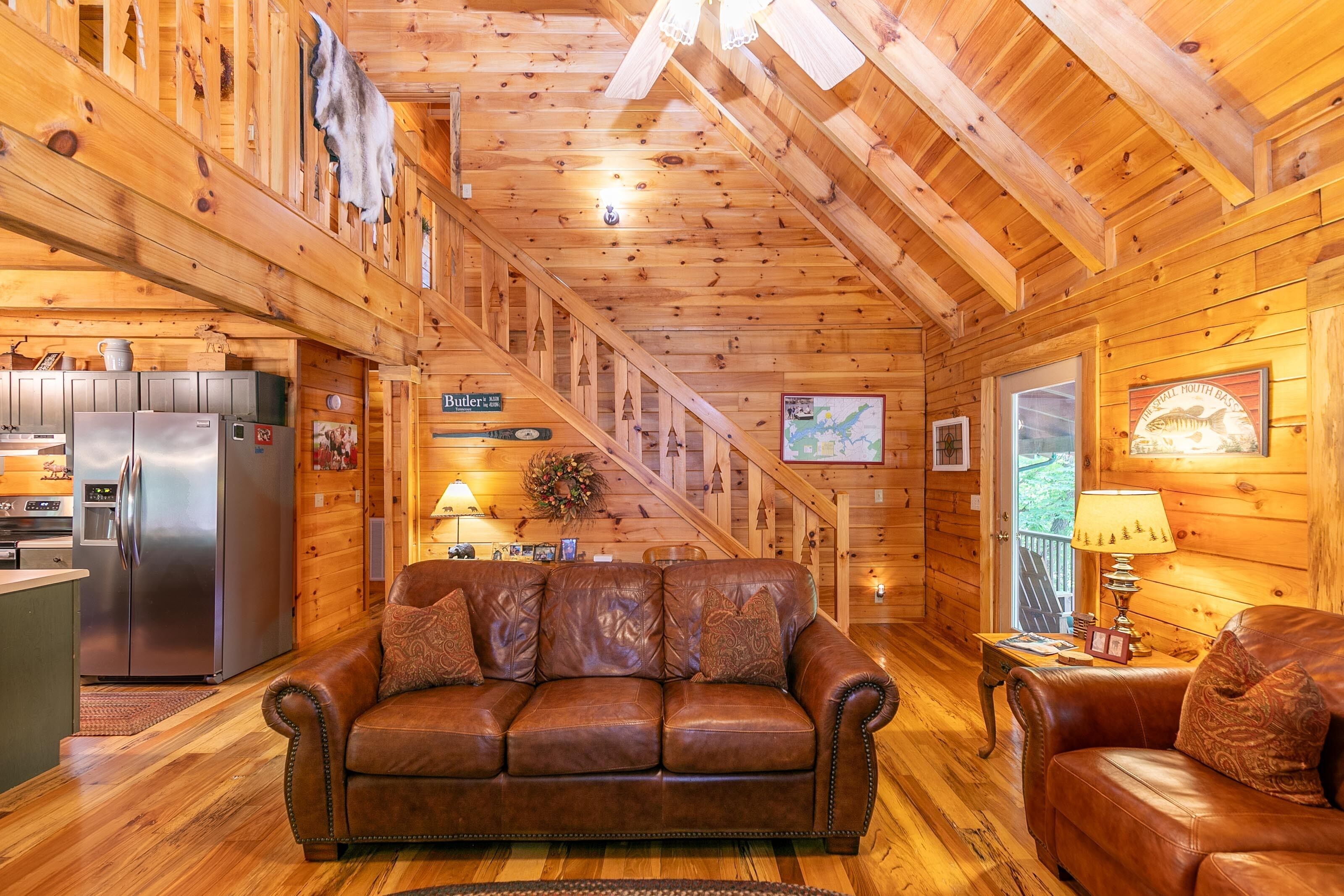 A cozy cabin interior with a wooden interior, a leather sofa, a dining table, and a kitchen area.