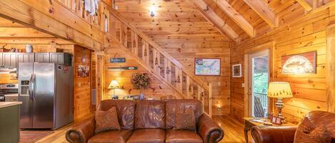 A cozy cabin interior with a wooden interior, a leather sofa, a dining table, and a kitchen area.
