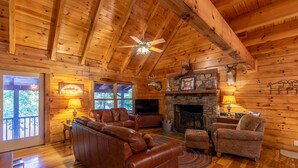 A log cabin interior with a stone fireplace, leather sofa, and a television. - Garretts Getaway at Watauga Lake - Private Dock, Lakefront (Butler)