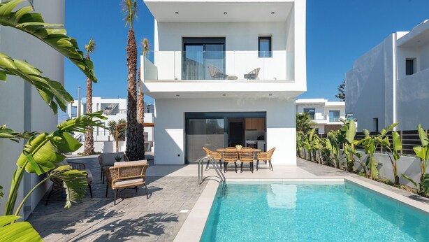 Un bâtiment moderne à deux étages doté d’une piscine, d’un espace extérieur aménagé et de plantes tropicales.