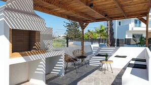 Une terrasse extérieure dotée d’une pergola en bois, d’un revêtement de sol en pierre et d’un espace détente avec des chaises et une petite table.