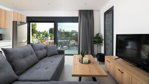 Un salon moderne comprenant un canapé, une table basse, un téléviseur et une porte-fenêtre coulissante donnant sur un espace extérieur.