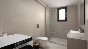 Une salle de bain moderne avec une douche à parois de verre, des toilettes, un lavabo et un lave-linge.