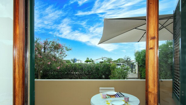 A balcony with a table set for dining, a large umbrella, and a view of the sky and surrounding greenery. - Seaside Suite with Terrace (Marina di Massa)