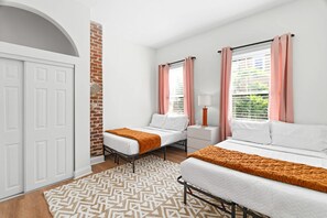 A hotel room with two beds, a brick wall, a white door, and a patterned rug. - The Laura | Entire Historic Home | Main St (Jacksonville)