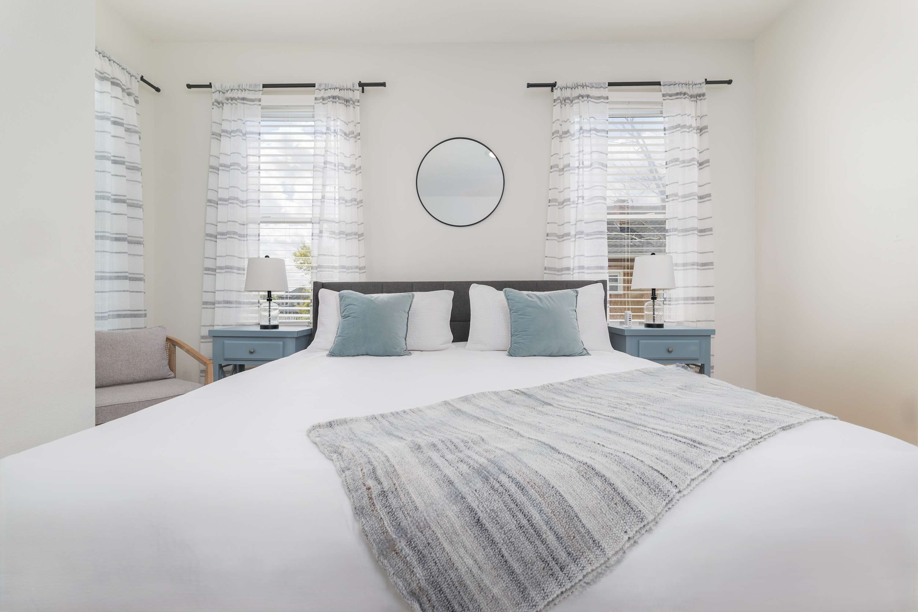 Une chambre à coucher avec un grand lit, deux tables de chevet, un miroir rond et des rideaux à rayures.