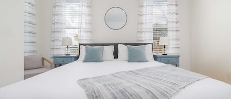 A bedroom with a large bed, two nightstands, a round mirror, and striped curtains.