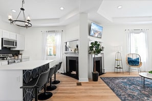 Una cocina moderna con una isla central, taburetes de bar, chimenea y un ventanal grande.