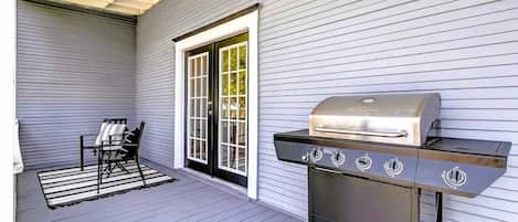 An outdoor patio with a grill, a chair, and a door.