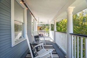 Une véranda couverte avec des balustrades blanches et un espace détente comprenant deux chaises et un banc.