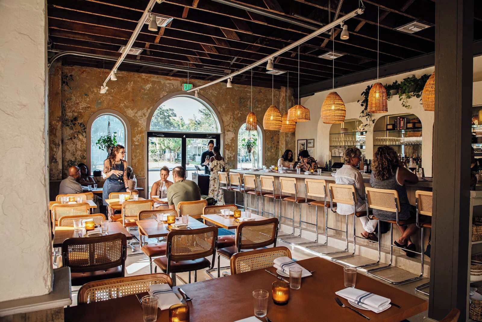 L’intérieur d’un restaurant se caractérise par de hauts plafonds, des poutres apparentes et une lumière naturelle abondante provenant de grandes fenêtres.