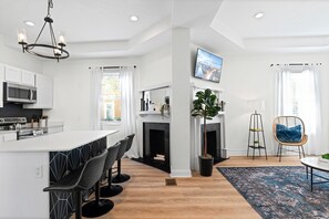 A modern kitchen with a central island, bar stools, a fireplace, and a dining area with a chair and table. - Designer 2BR | Historic Charm + Walk to Fun (Jacksonville)