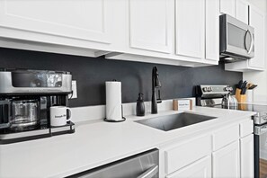 A modern kitchen with white cabinetry, a coffee maker, a sink, and a microwave.
