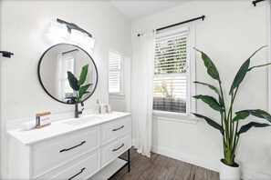 A bathroom with a white vanity, a round mirror, a modern faucet, and a potted plant.