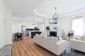 A modern living room with a sofa, a dining area with chairs, a kitchen with white cabinets, and a fireplace. - Designer 2BR | Historic Charm + Walk to Fun (Jacksonville)